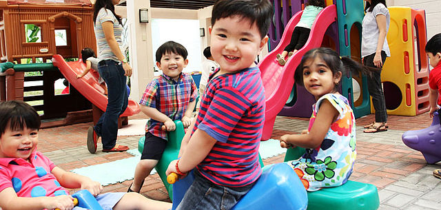 Children playing on plastic rockers in a classroom setting.