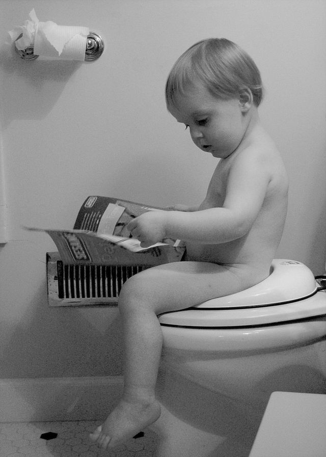 A boy reading while sitting on the toilet