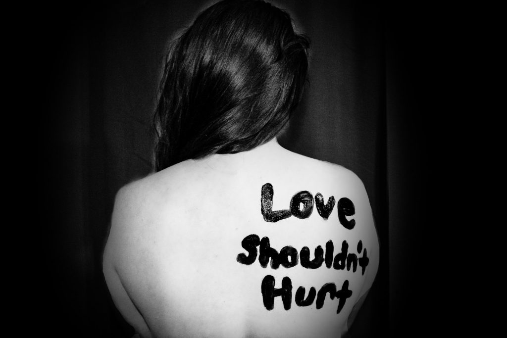 A black and white image of a woman with "Love Shouldn't Hurt" painted on her back