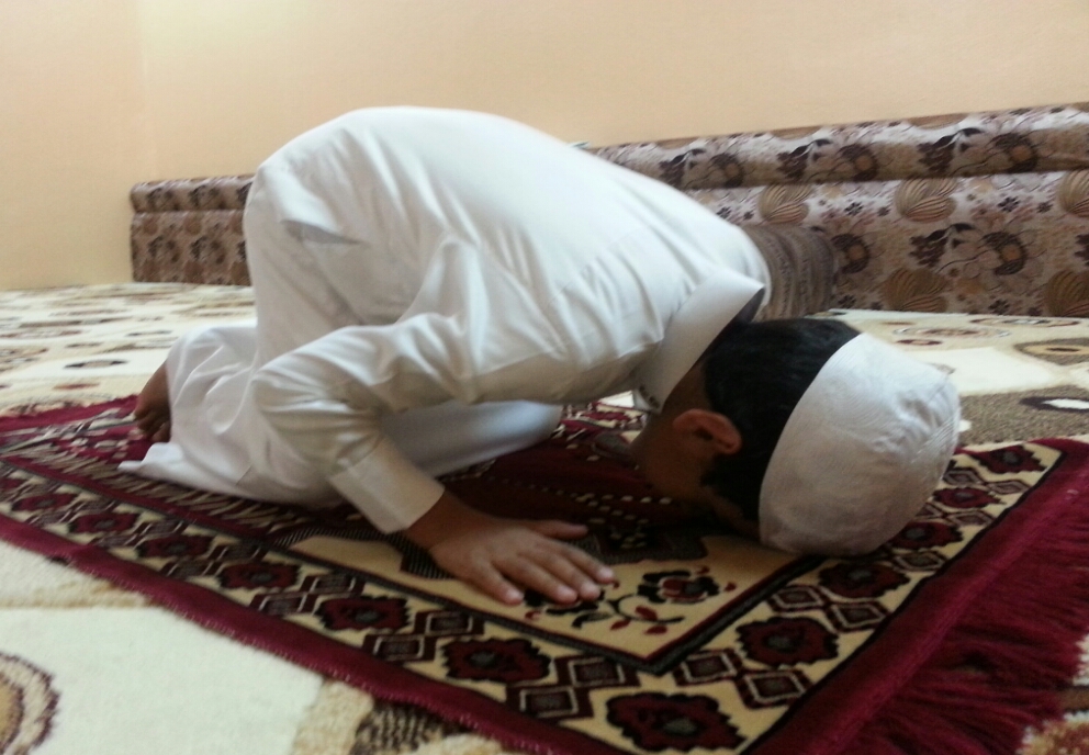 A Muslim boy praying on a prayer rug