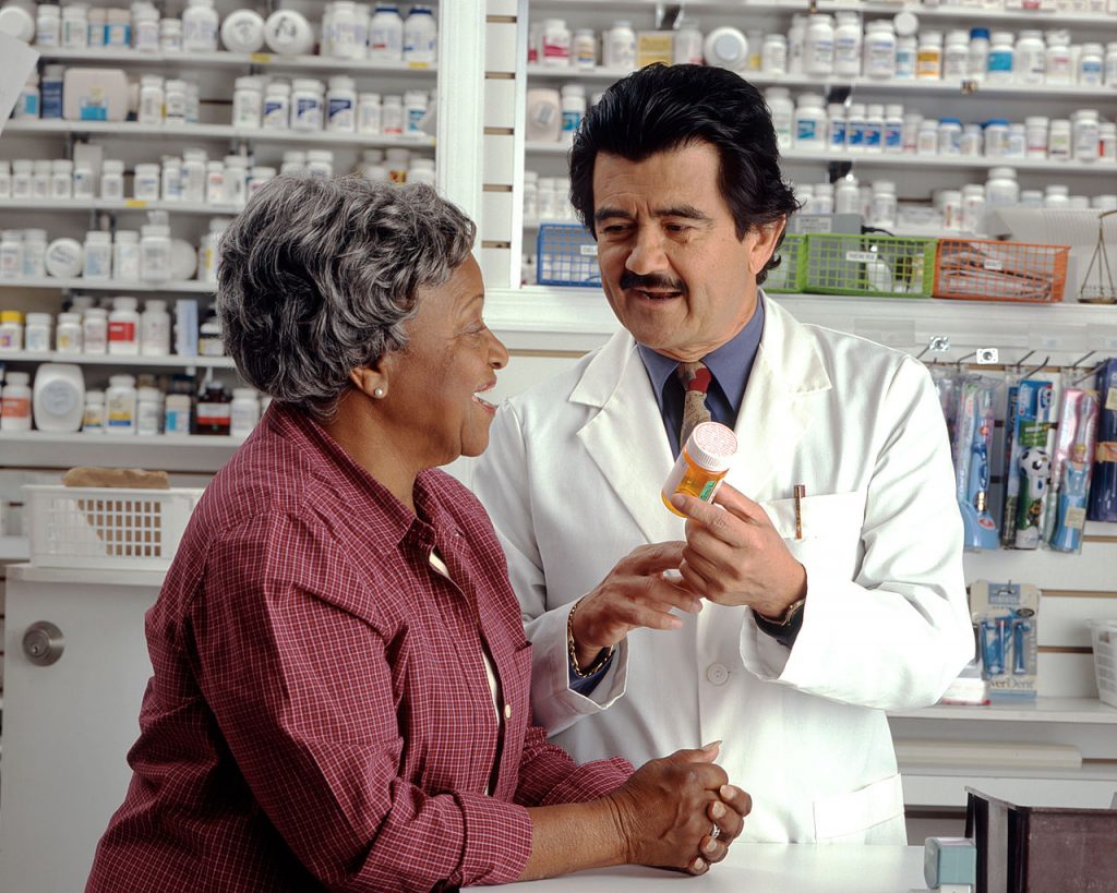 A pharmacist holding a bottle of medication while talking with an elderly woman.