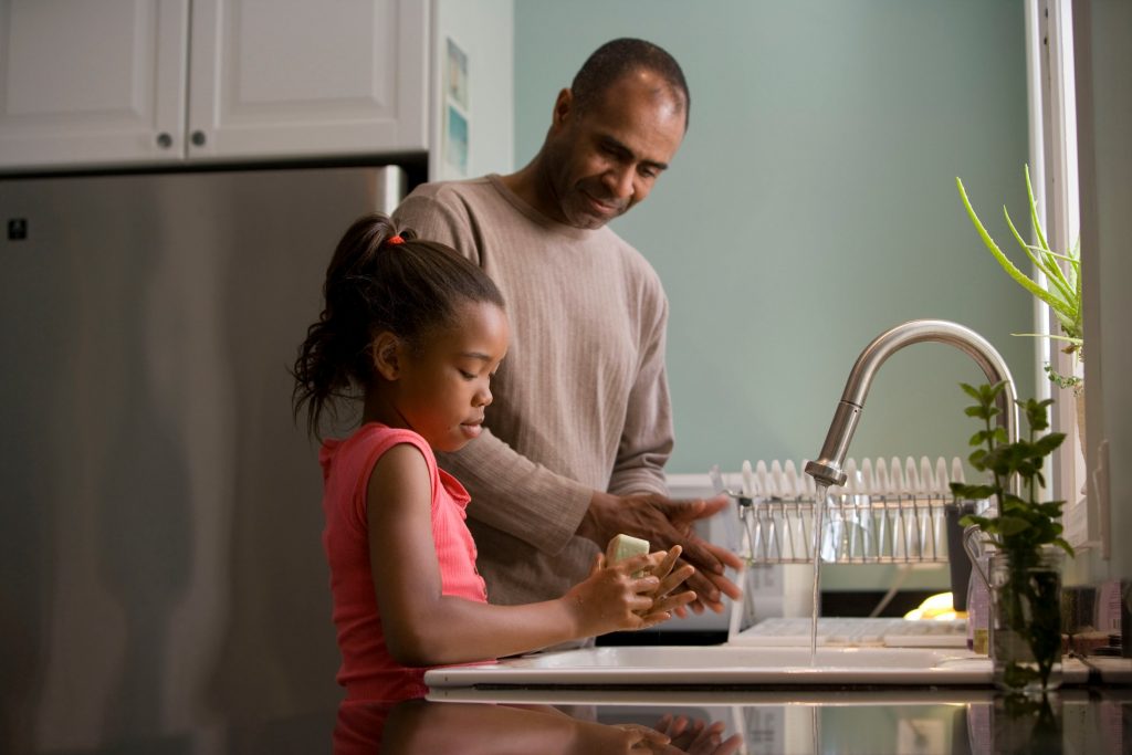 A father showing his daughter how to wash her hands by example