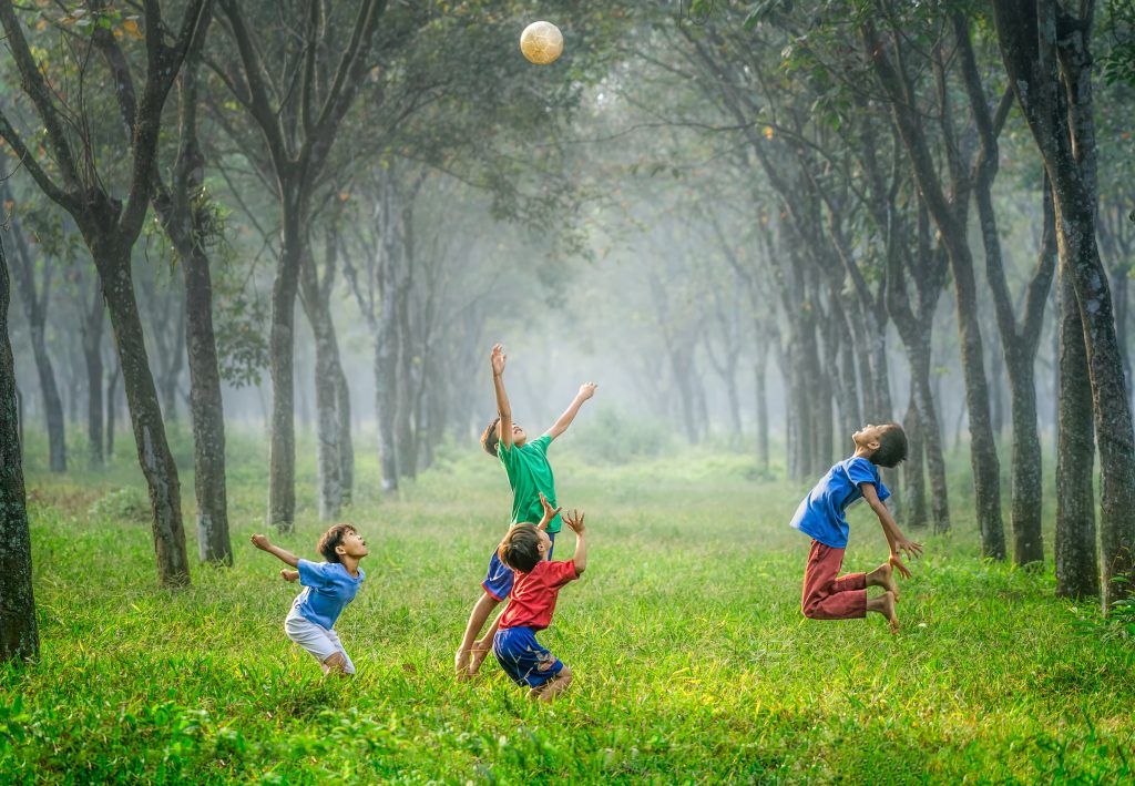 Four boys playing together in a forest with a ball