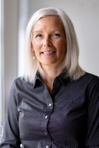 Brenda Knights headshot. Middle aged woman with white hair and symmetrical oval shaped face wearing a black buttoned up shirt