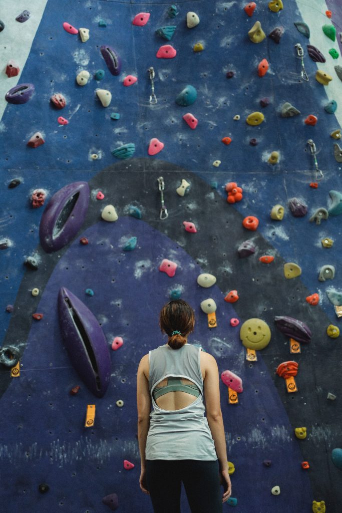 Person stands at the bottom of a tall climbing wall planning their route.