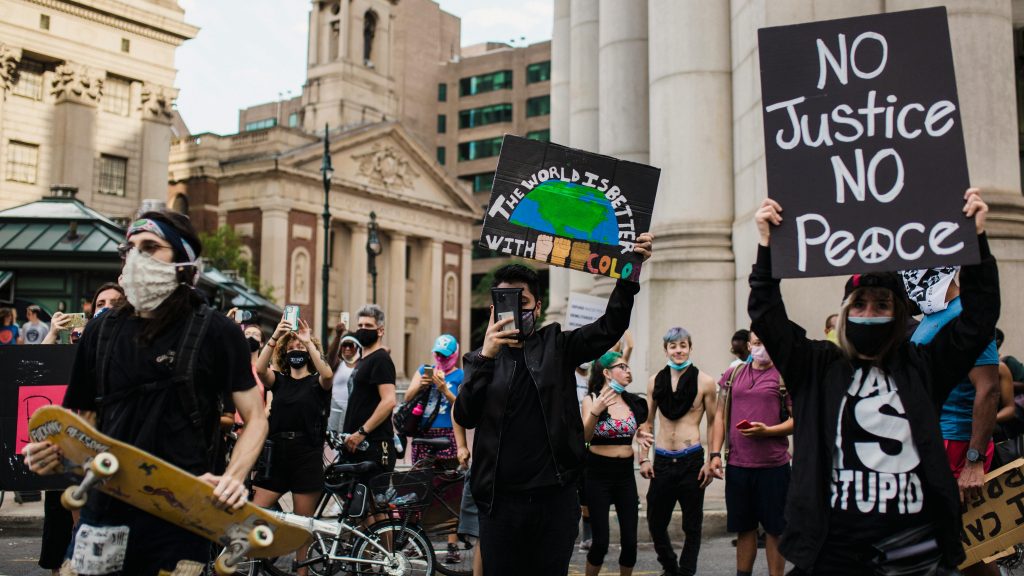 A protest with obscured faces, signs about Earth and justice, and a person holding a skateboard.