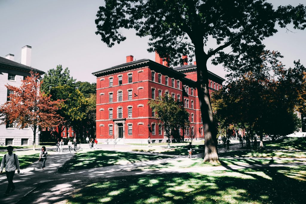 Campus scene with a red brick building, green trees, and students walking on a sunny day.