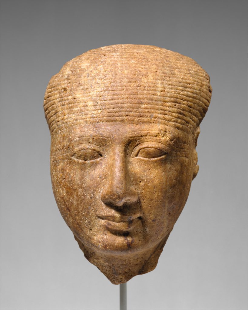 A bright coloured gold-tone statue of a head. The head is missing some fragments from where the ears should be. Some discoloration is found over the face.