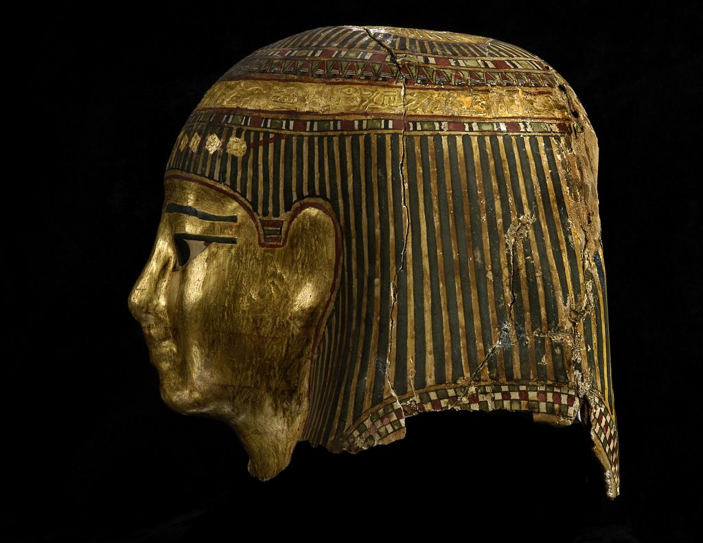 A side profile (facing left) of a mummy mask. The mask is black and gold in colour.