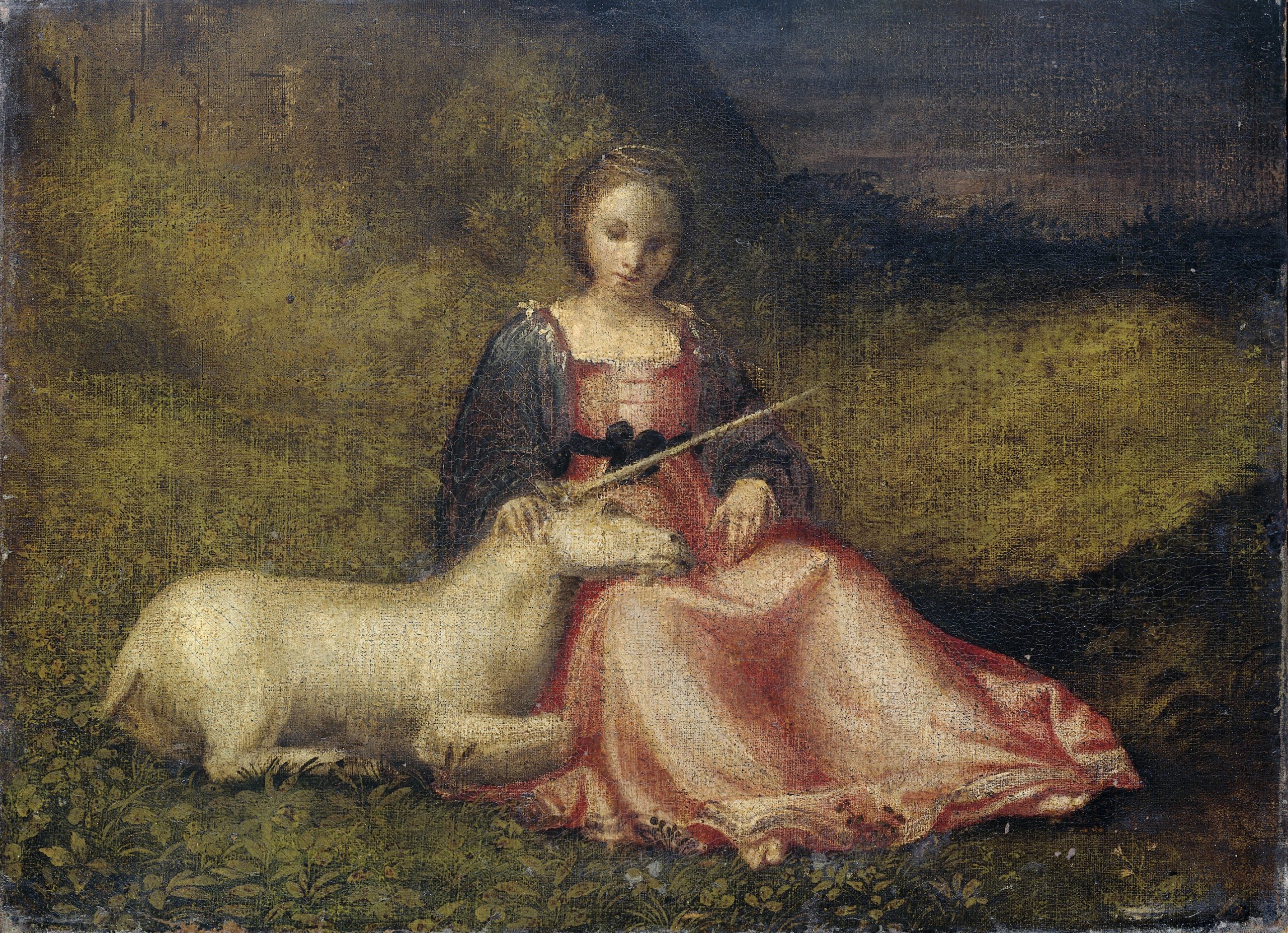 A young woman sits on the ground and looks down towards a unicorn resting in her lap.