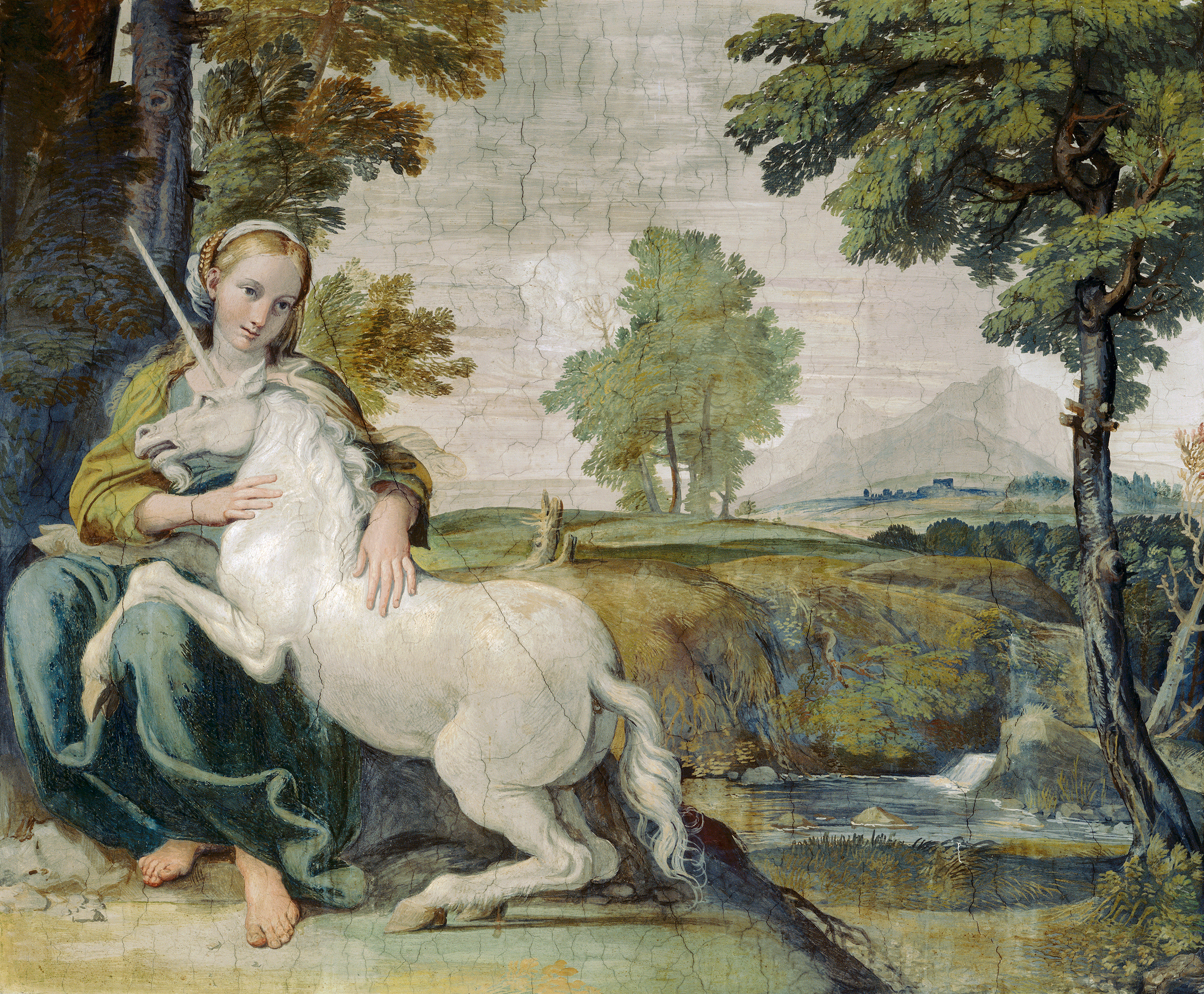 A barefoot young woman sits on a tree with a unicorn in her lap surrounded by hills and trees.