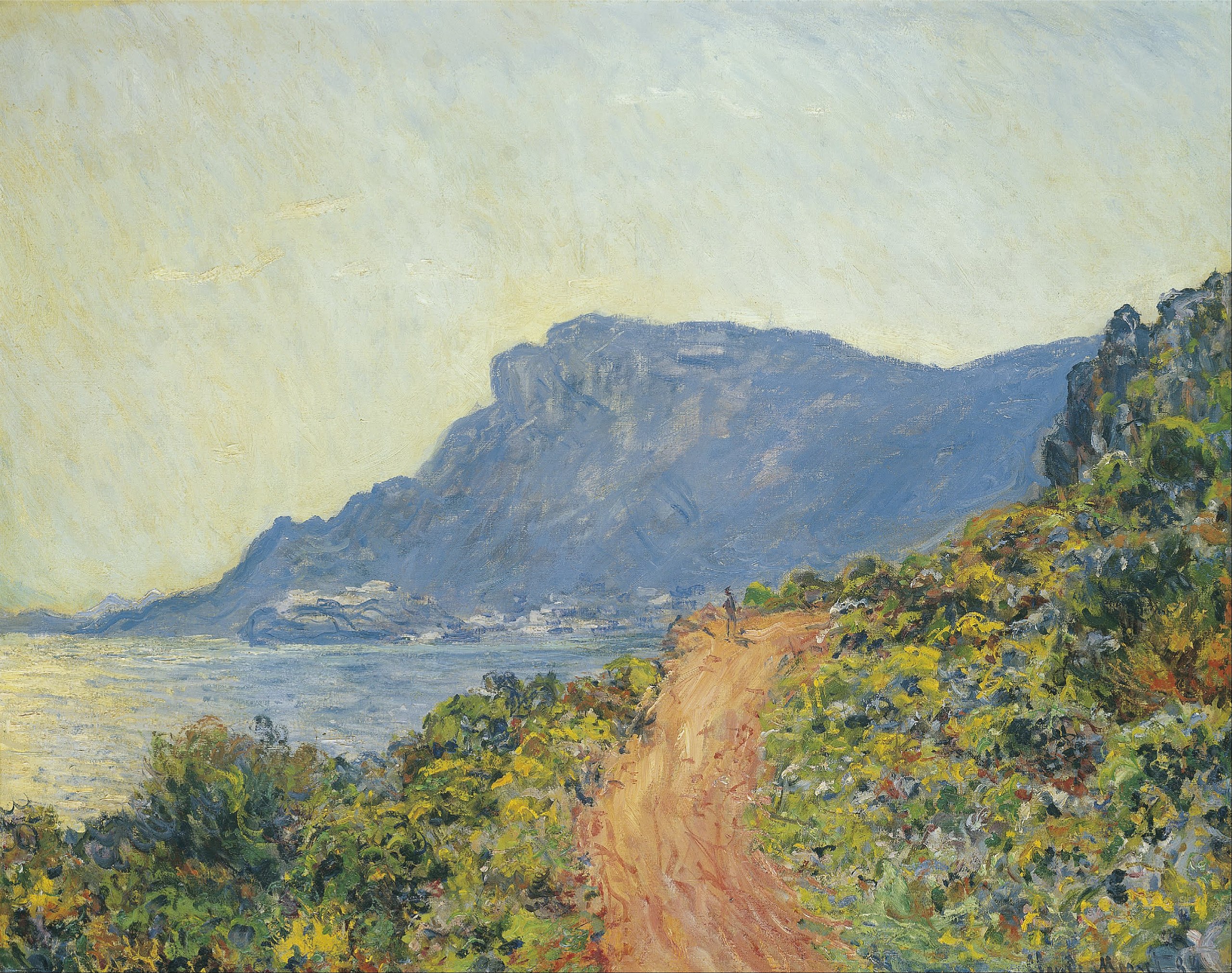 A landscape view of a small dirt road in a grassy area overlooking the sea with a mountain in the distance