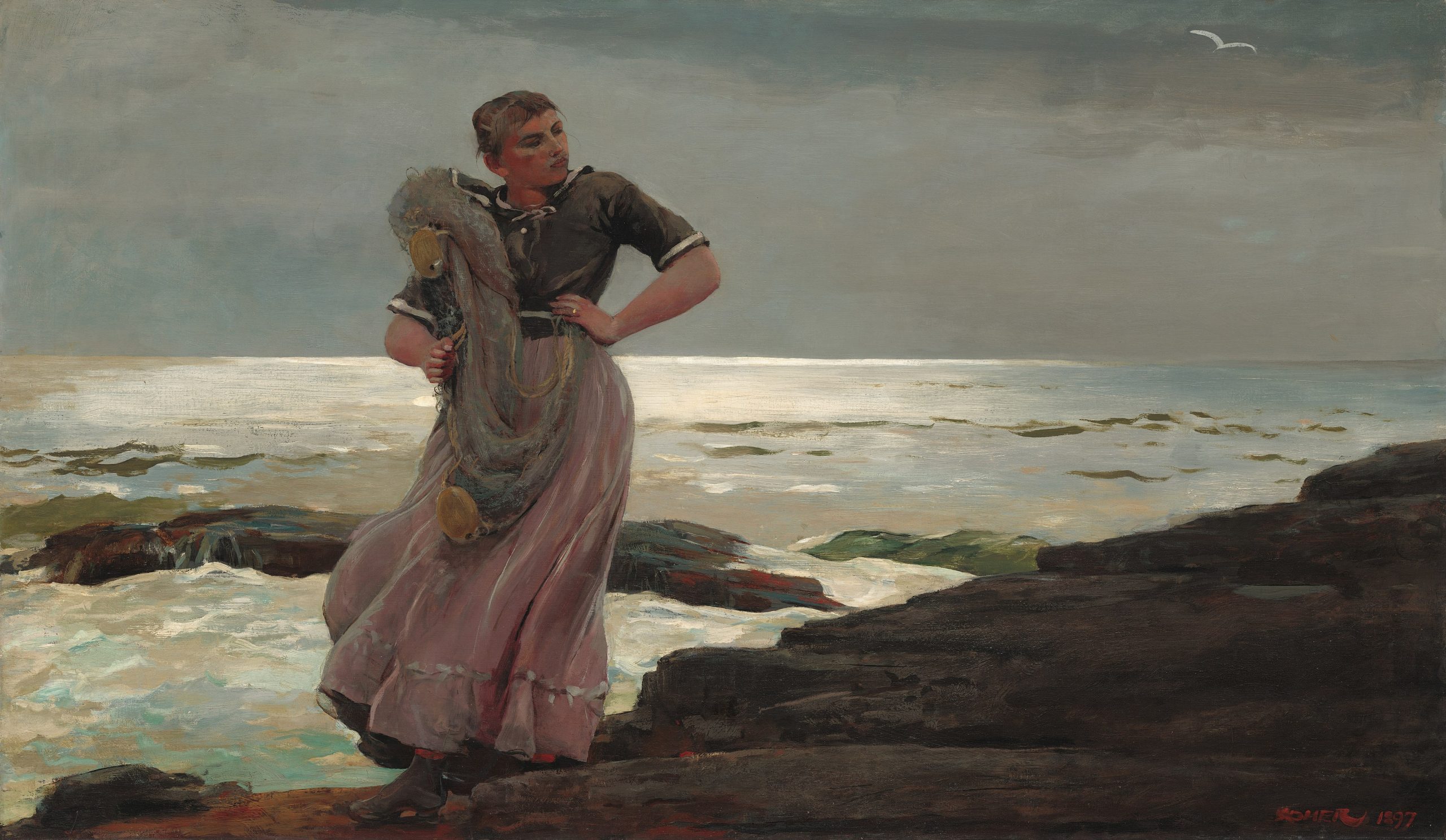 A woman standing on a rocky shoreline gazing to her left with a fishing net and buoys slung over her shoulder