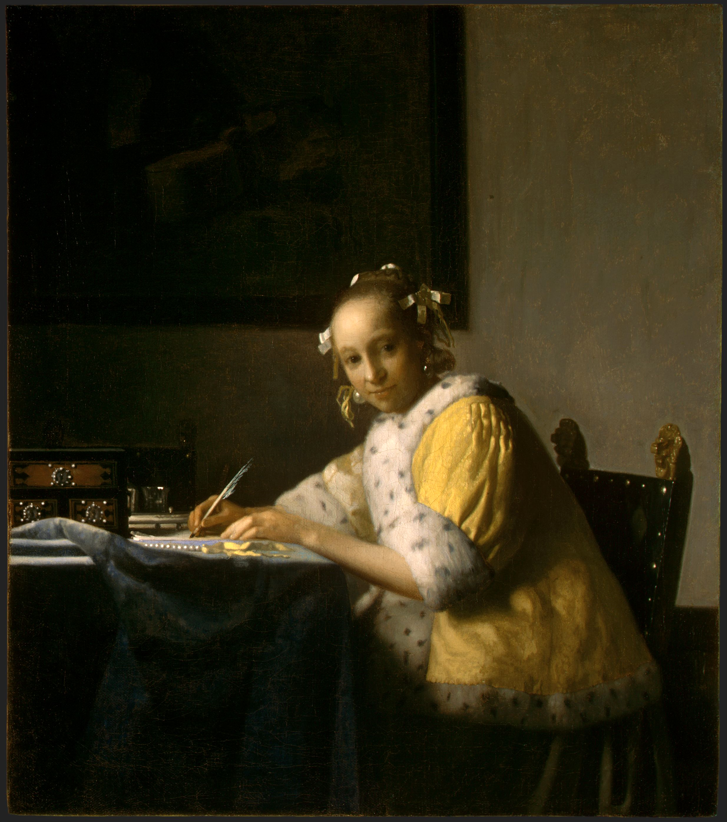 A woman looking back at the viewer writing a letter on a desk