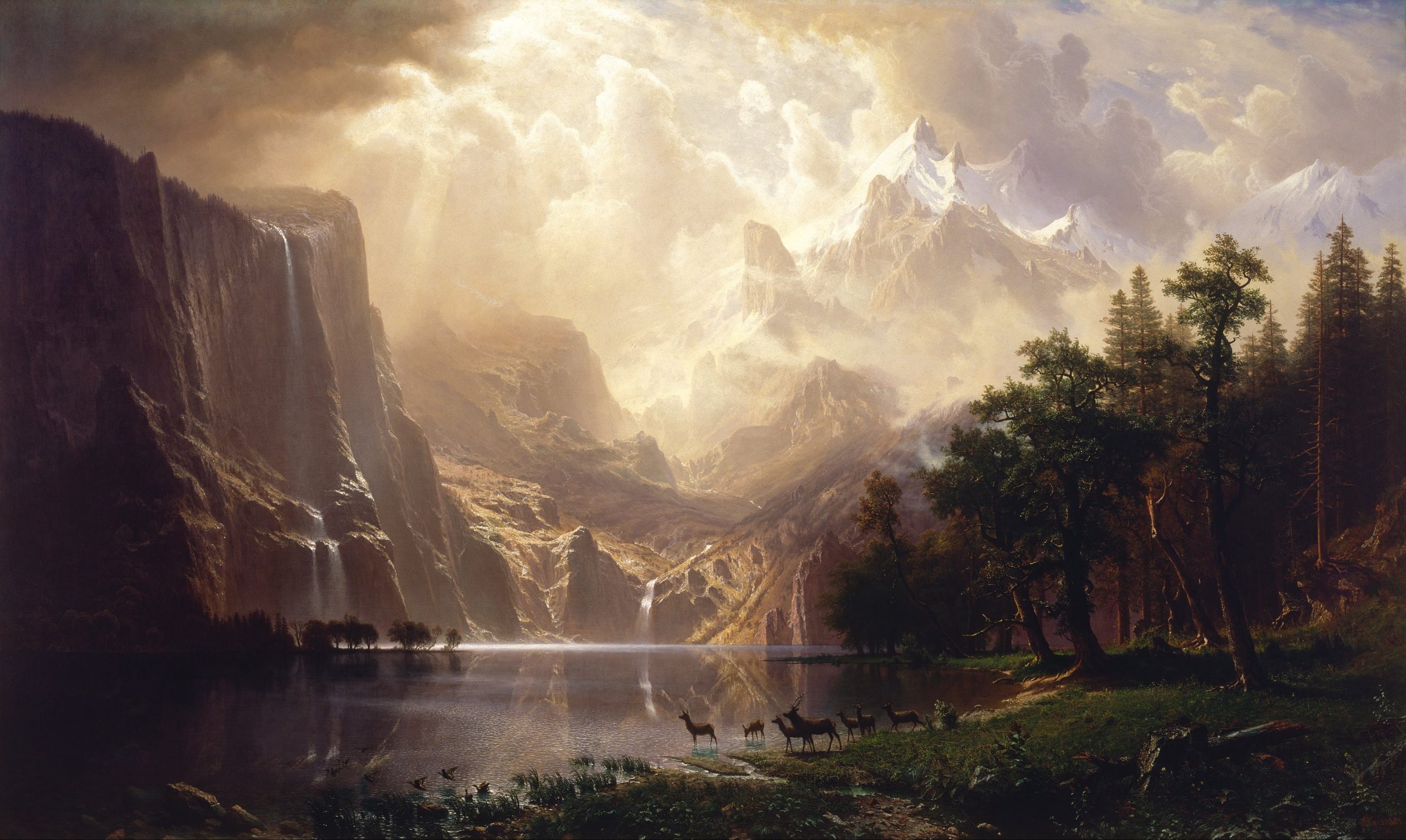 A landscape view of sunlight shining upon mountains overlooking a clear lake beside the woods