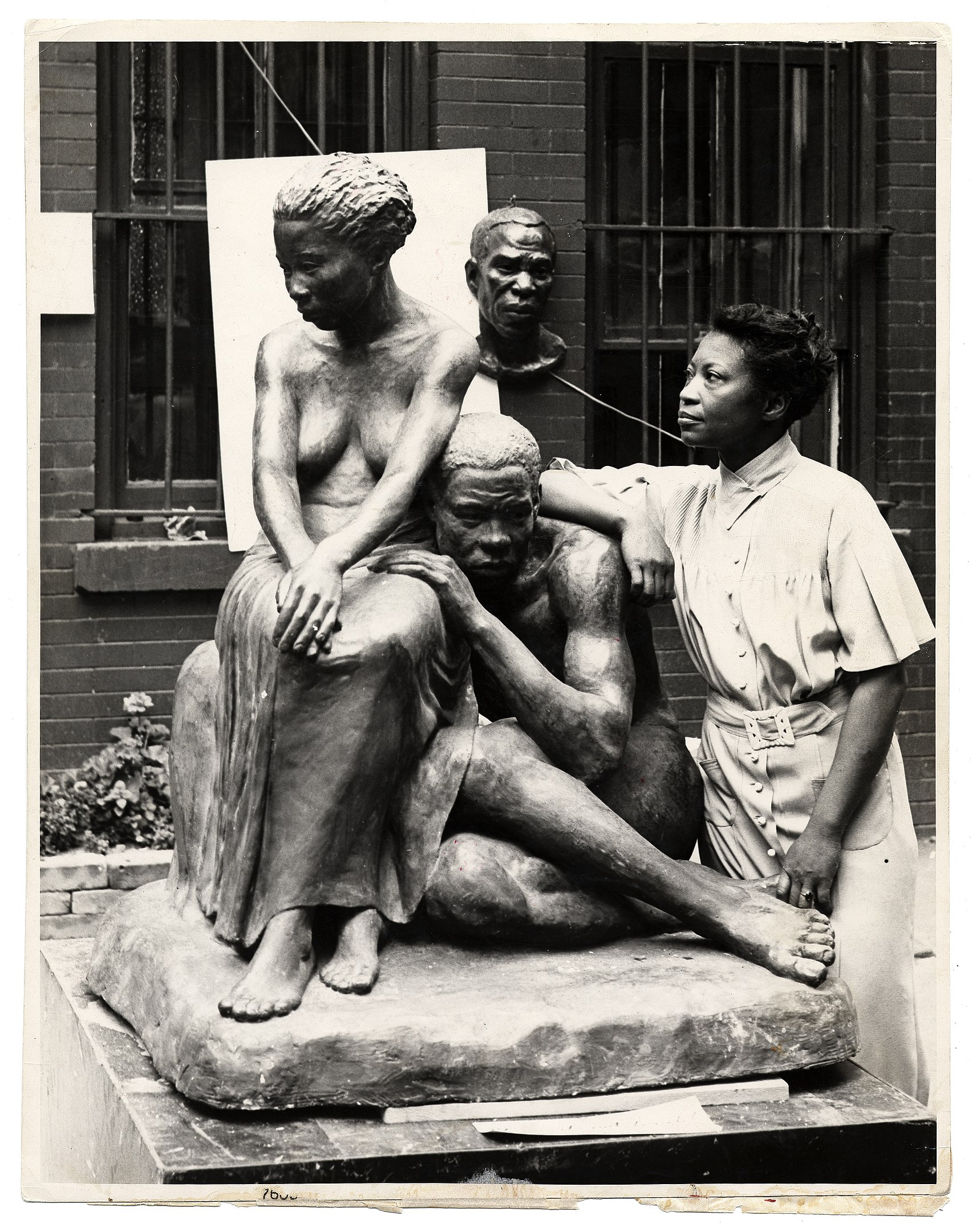 A photograph depicting an artist standing next to her figurative sculptures