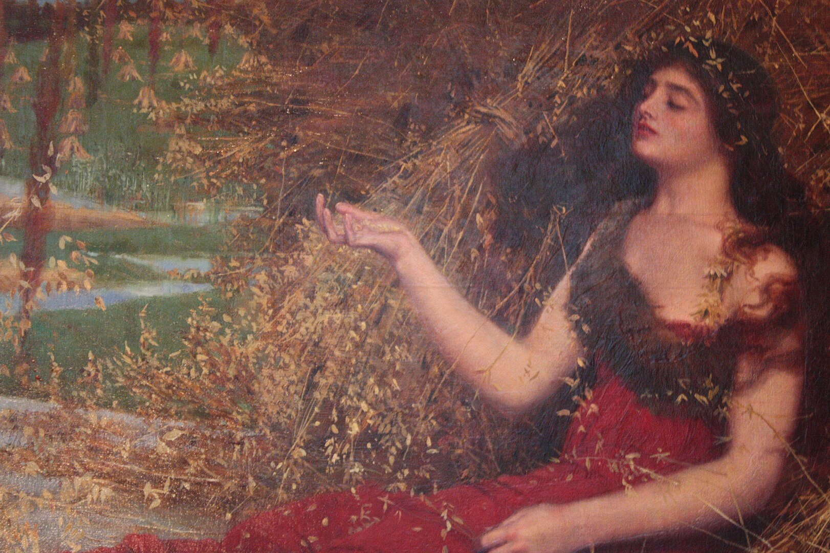 A woman with her eyes closed and her right arm lifted leans against foliage in an autumn landscape.