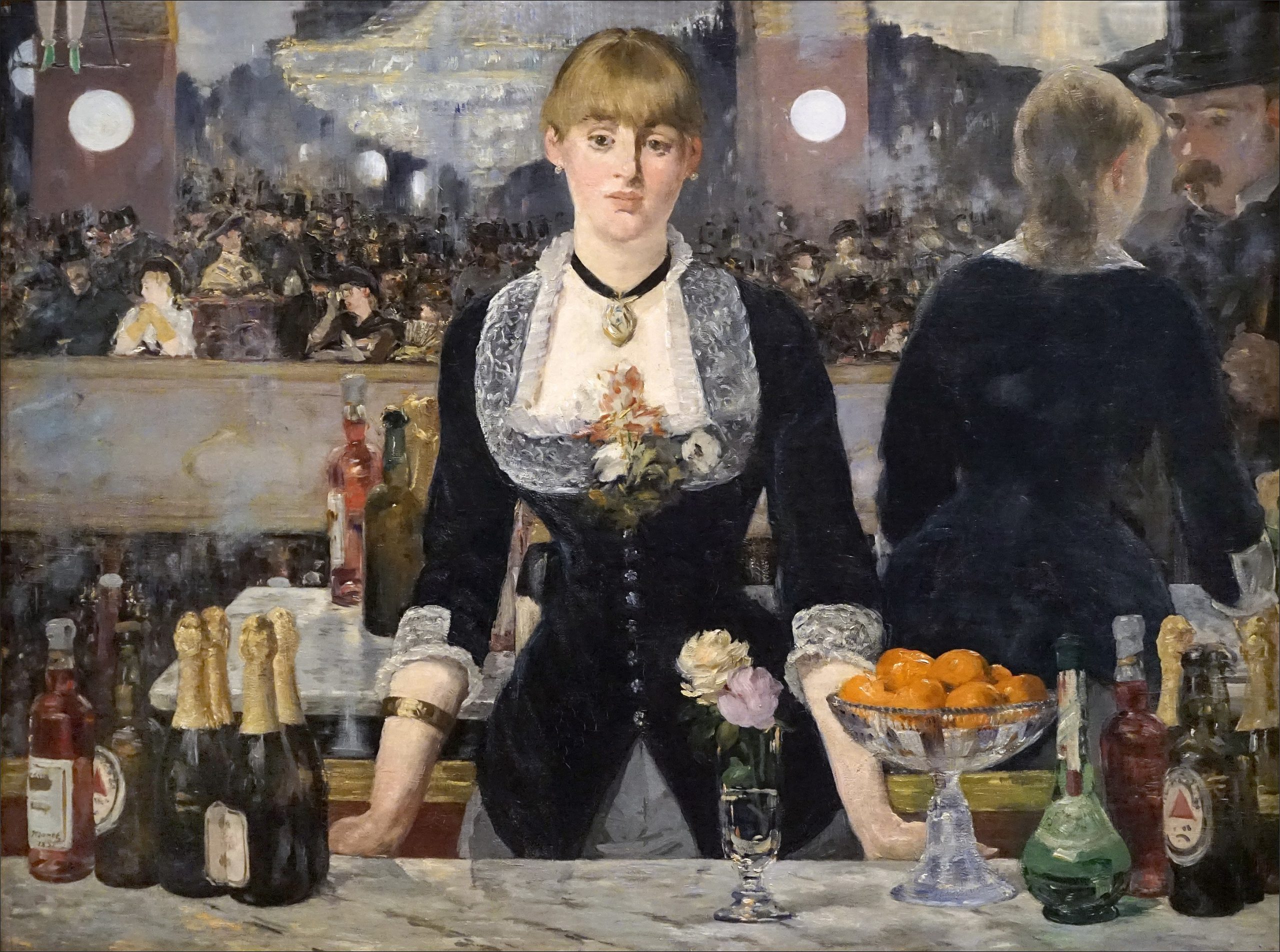 A female bartender leaning on a marble countertop filled with alcoholic drinks while looking back at the viewer