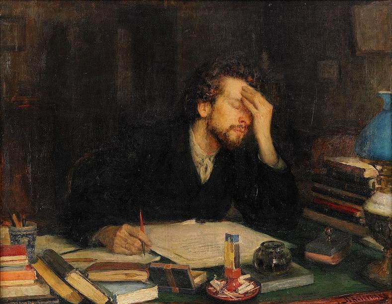 A man holding a pen in one hand facepalming while seated at a desk cluttered with books