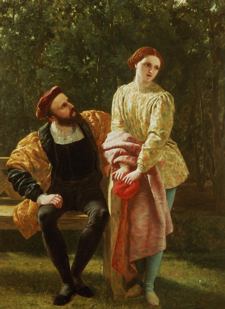 A man sits on a bench in a forest while looking up at the woman who stands next to him.