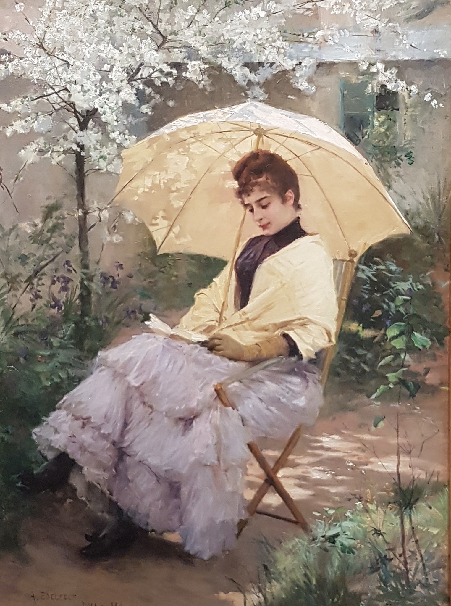 A woman with a parasol sitting on a chair reading a book under the shade of a tree