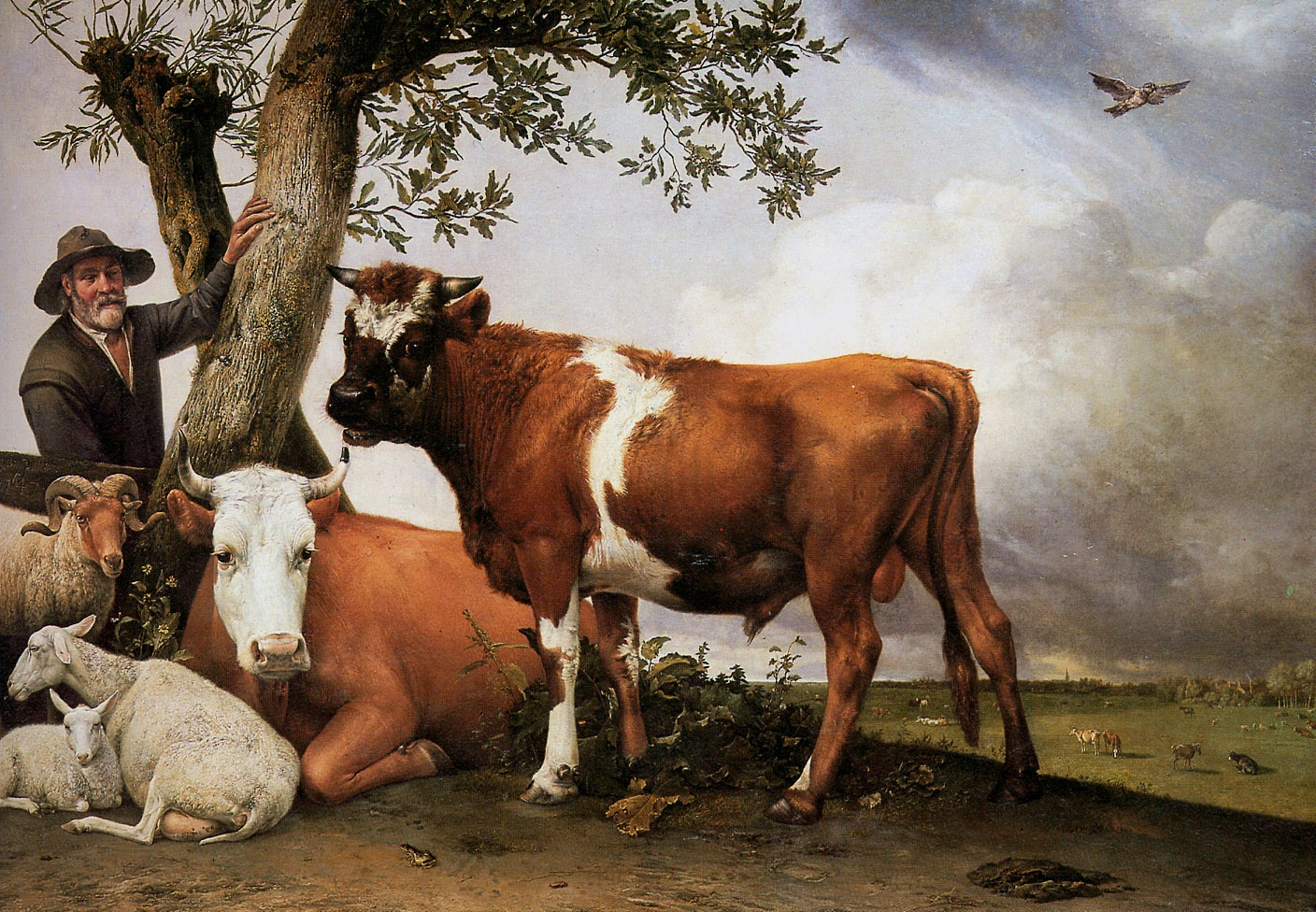 A couple of bulls rest by a tree while a man stands beside them to the left.