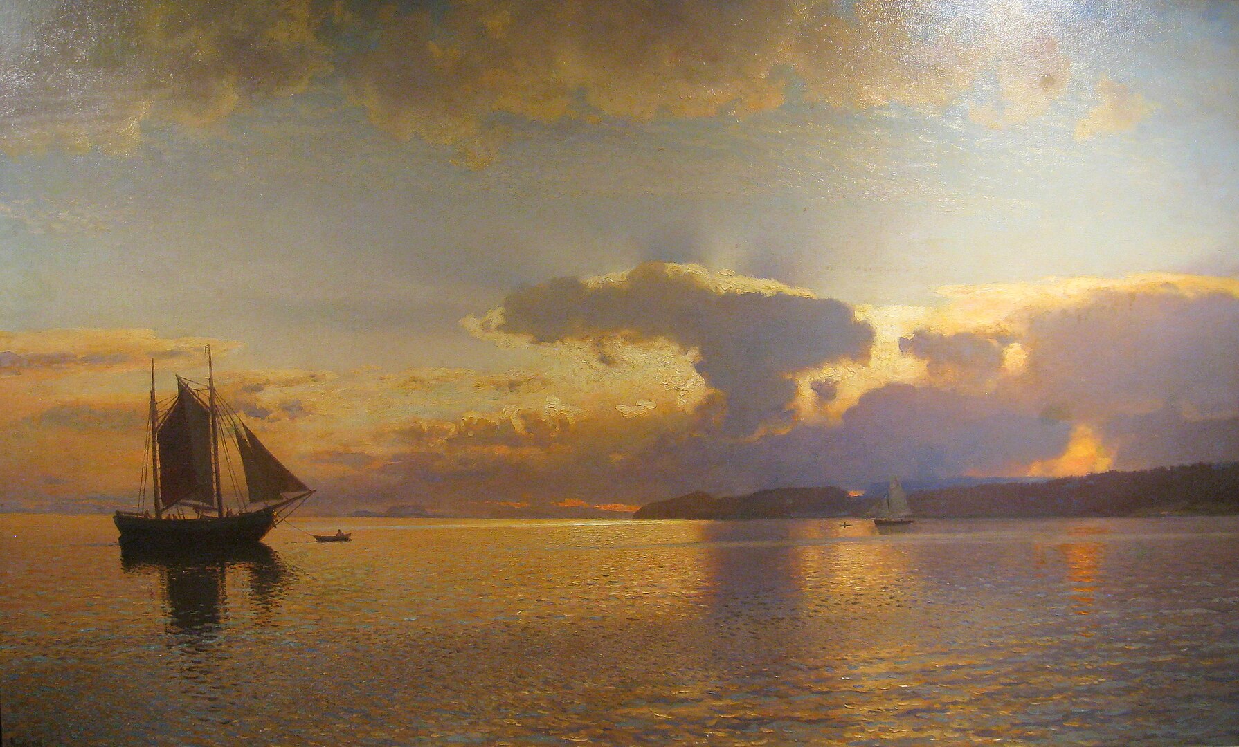 A landscape view of an ocean with several sailboats at sunset