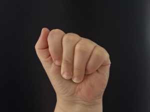 A hand in front of a black background. The hand is in a fist. The palm is facing the camera. The thumb is straight up. The four fingers are bent downwards and held close to the palm.