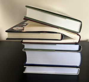 A stack of five books. Another book is inserted midway through the book second from the top.